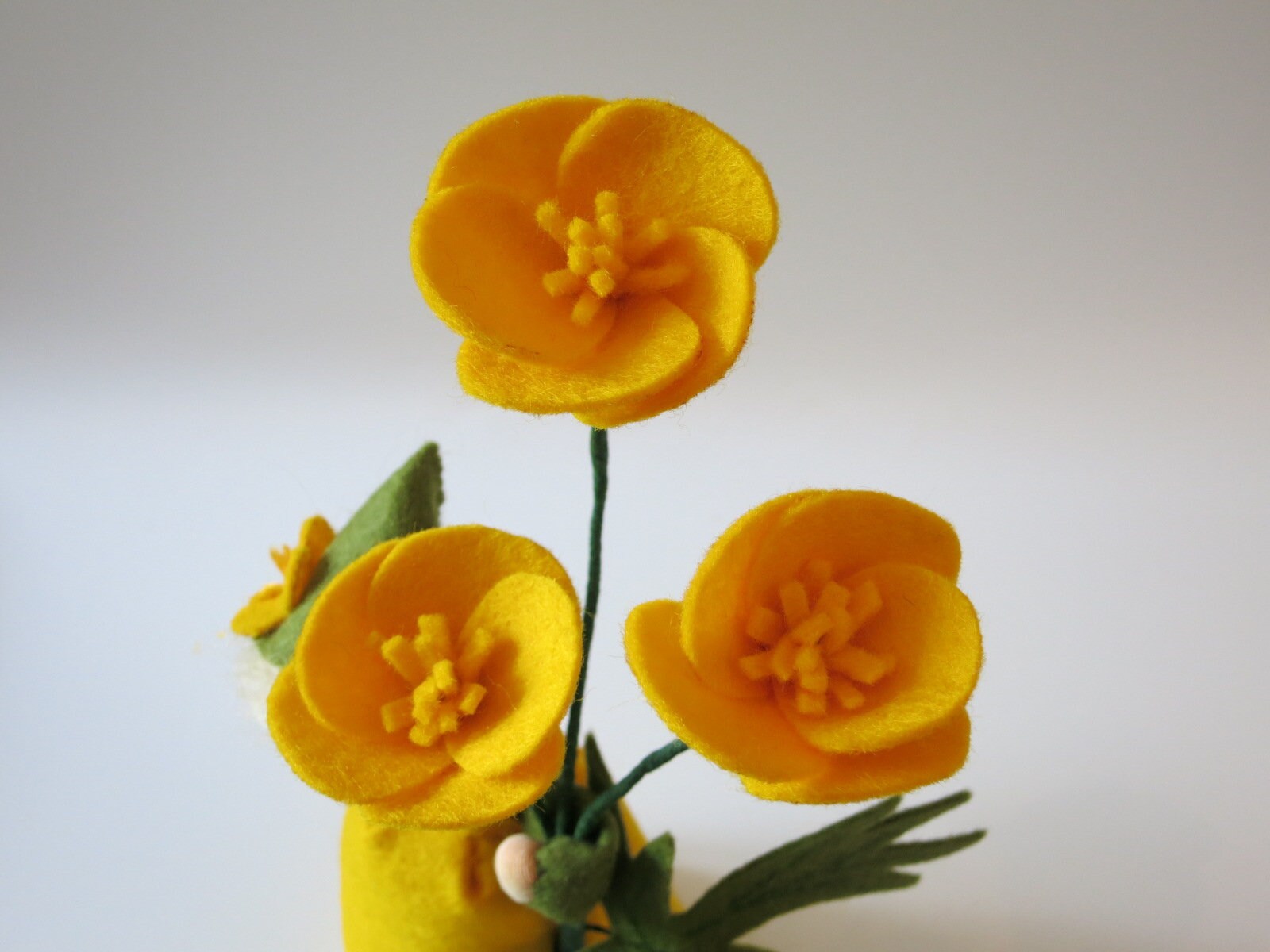 Detail von drei gelben Butterblumen aus Filz mit handgearbeiteten Blütenmitten und grünen Stielen