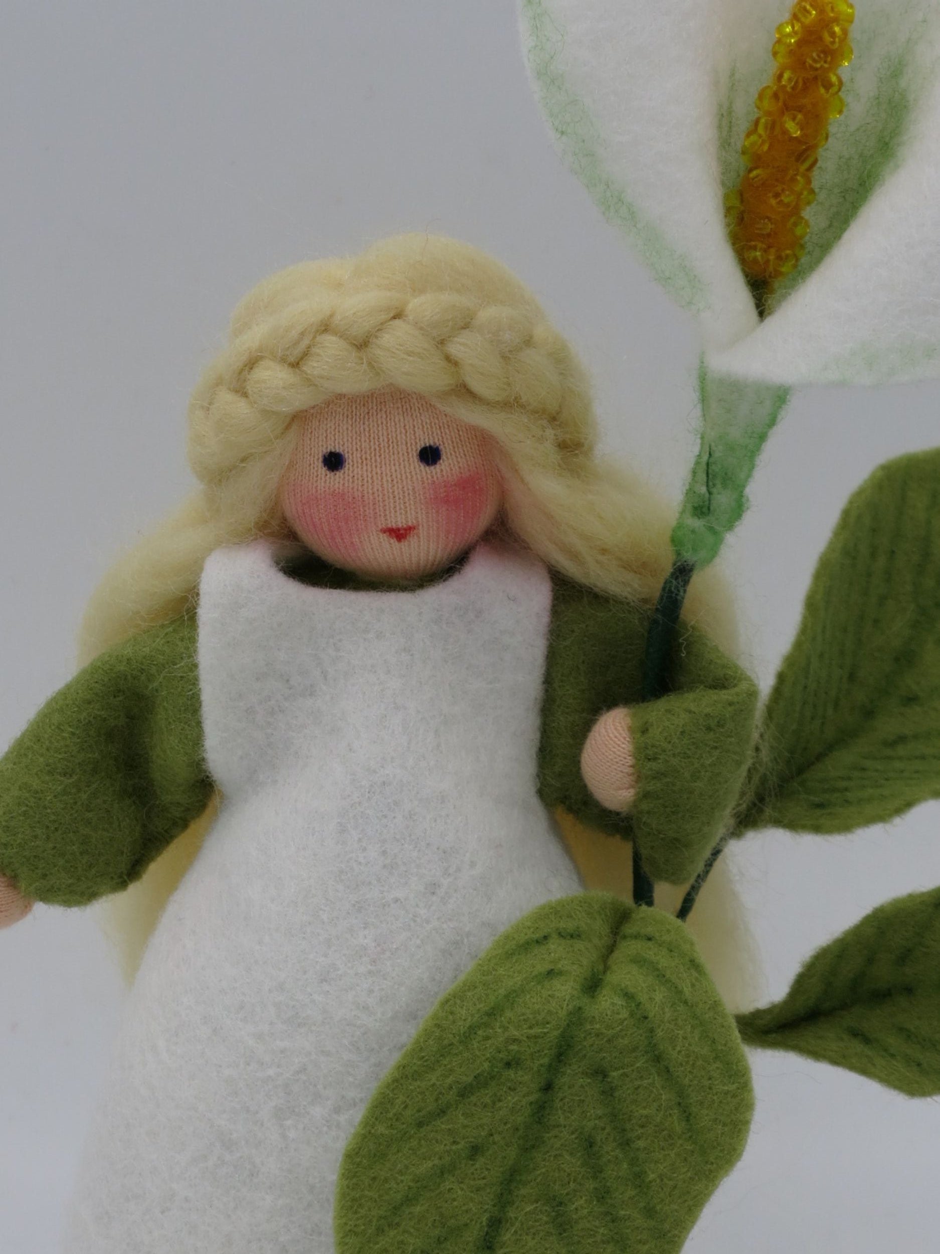Detail des Calla-Blumenkinds mit blondem Flechthaar, weißem Filzkleid, großer Blüte und strukturierten grünen Blättern