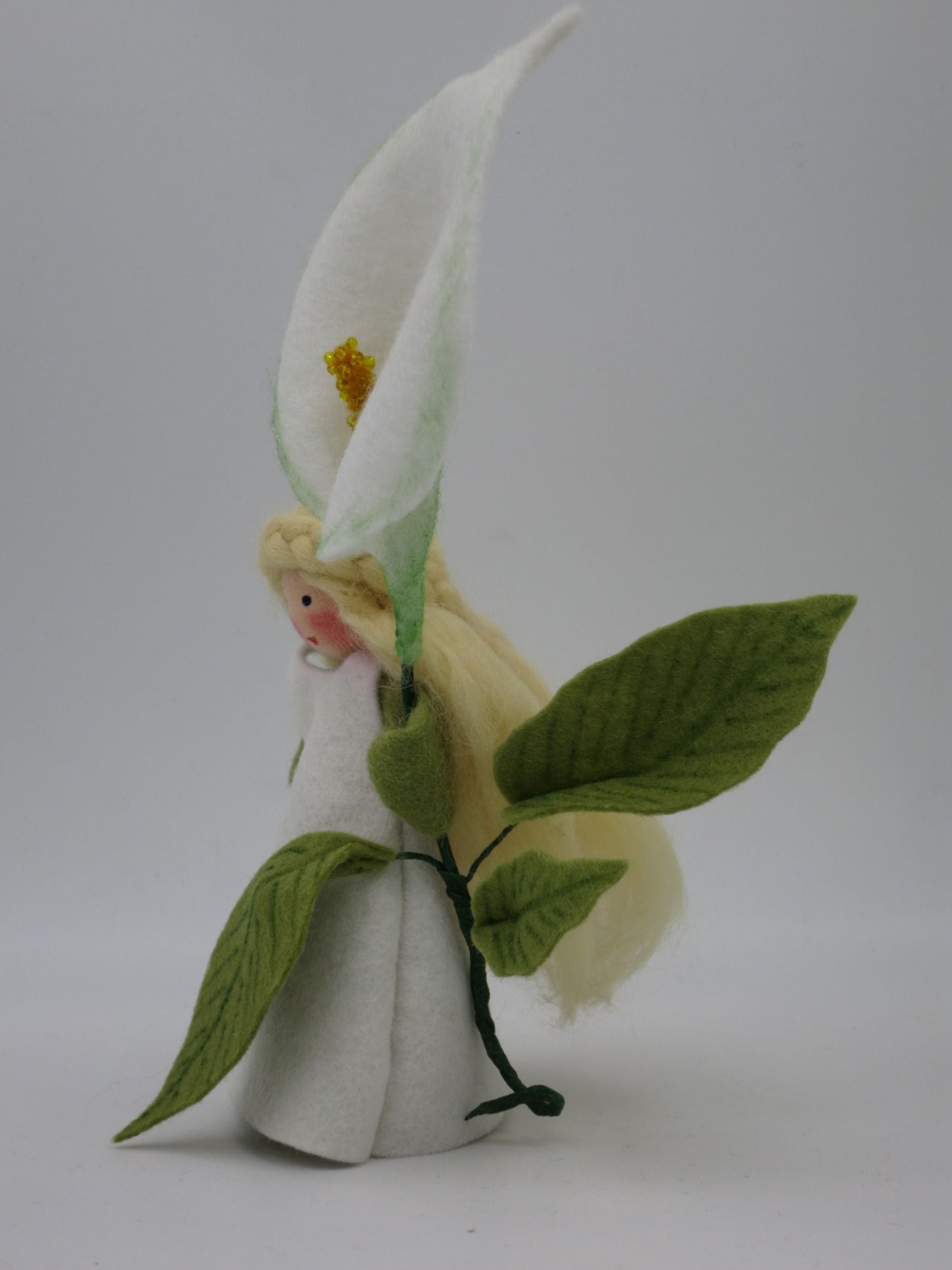 Seitliche Ansicht des Calla-Blumenkinds mit hoher weißer Blüte, blondem Wollhaar und großen grünen Filzblättern