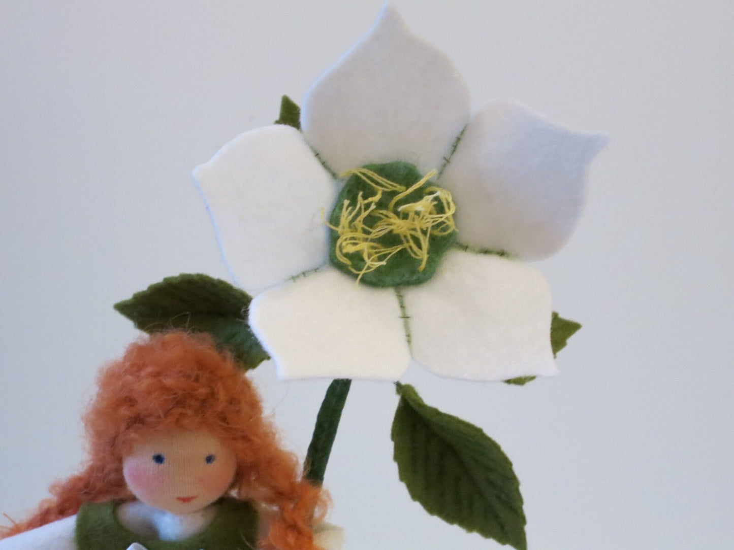 Weiße Christrosenblüte aus Filz mit grün-gelber Mitte neben dem rothaarigen Blumenkind für den Wintertisch