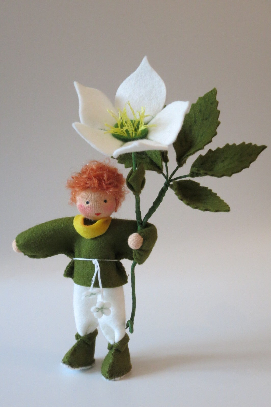 Christrosen-Blumenkind als Junge mit roten Haaren, grün-weißer Filzkleidung und großer weißer Winterblüte