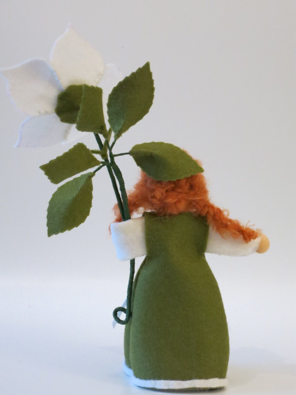 Rückansicht des Christrosen-Mädchens mit grünem Filzkleid, rotem Wollhaar und weißer Blüte mit Blättern