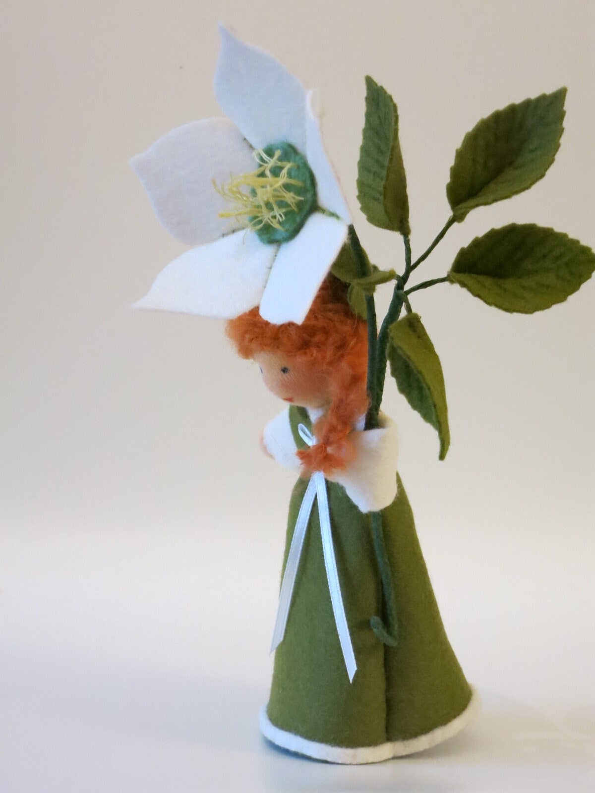 Seitliche Ansicht des Christrosen-Mädchens mit weißer Winterblüte, grünen Filzblättern und langem roten Haar