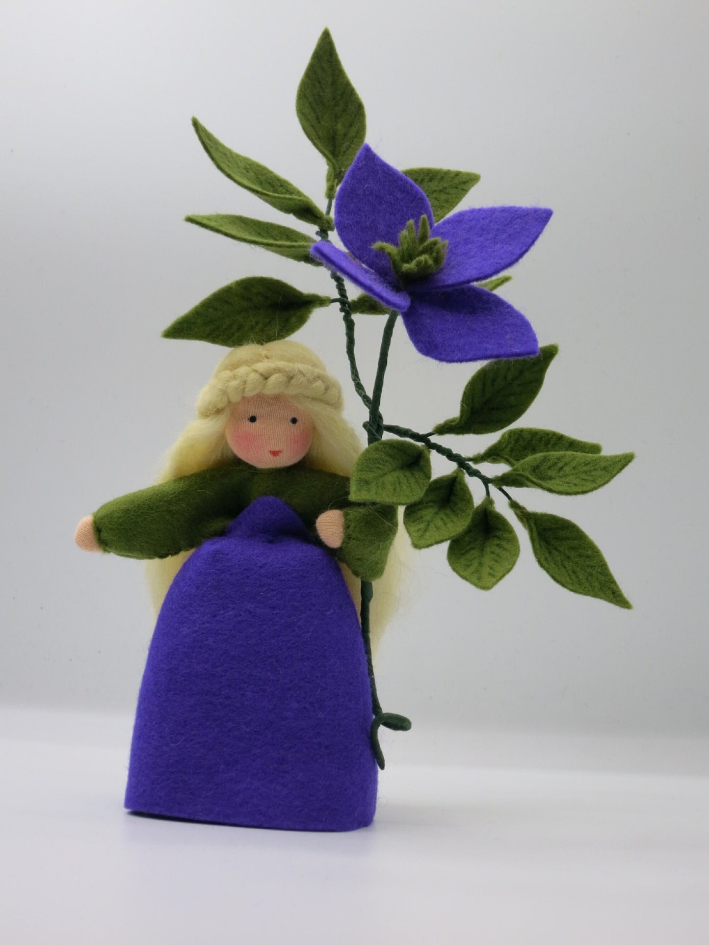 Clematis-Blumenkind frontal mit violettem Filzkleid, markanter Blüte und fein schattierten grünen Blättern