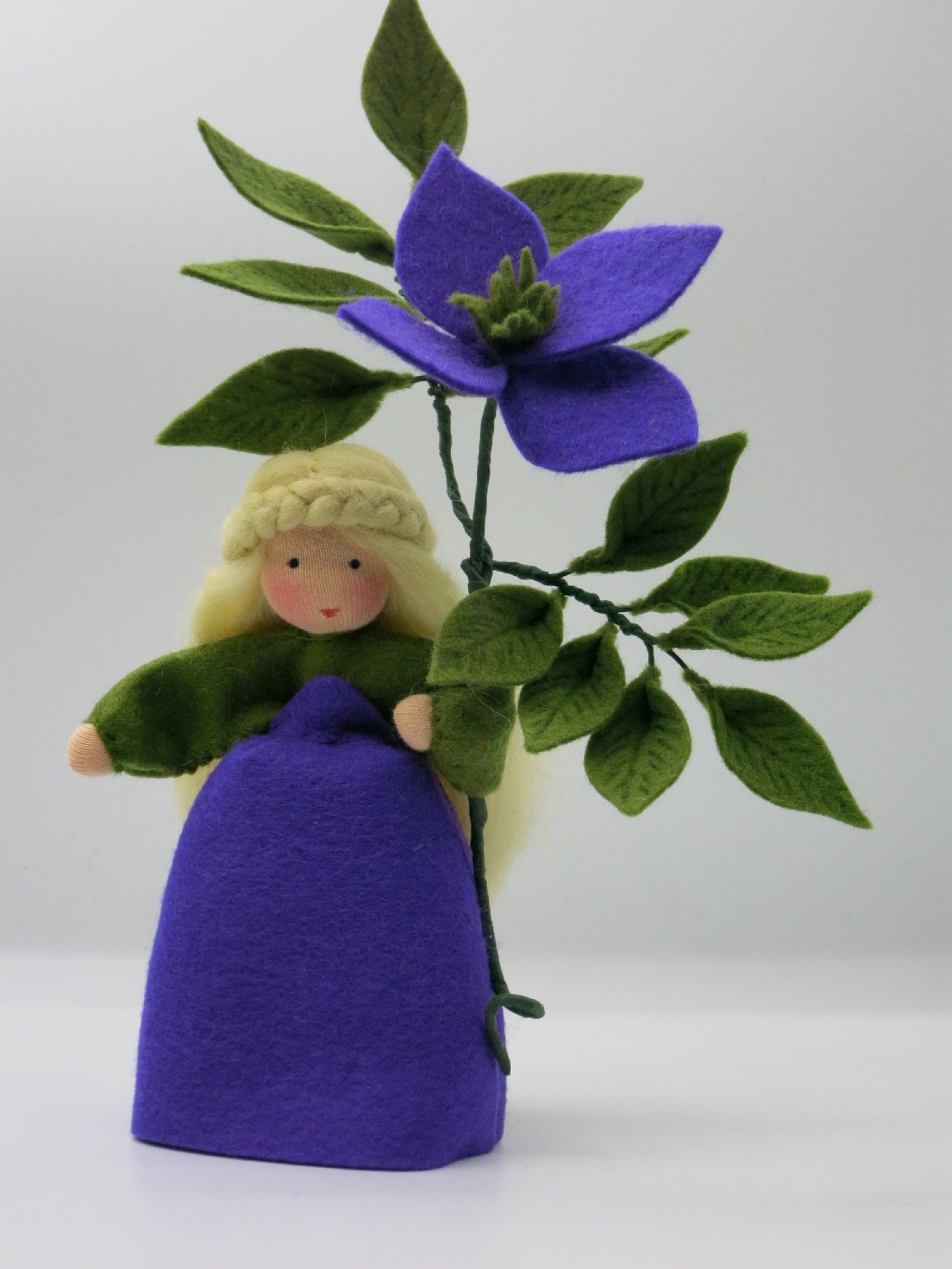 Clematis-Blumenkind frontal mit großer violetter Blüte, grünen Filzblättern und blondem Flechthaar für den Sommer