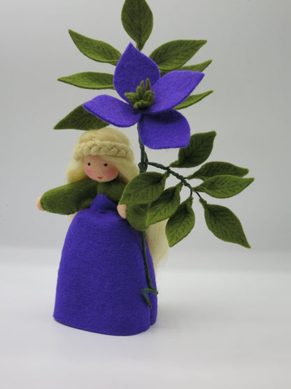 Clematis-Blumenkind mit violetter Filzblüte und grünem Blätterzweig, handgefertigt für den Waldorf-Jahreszeitentisch