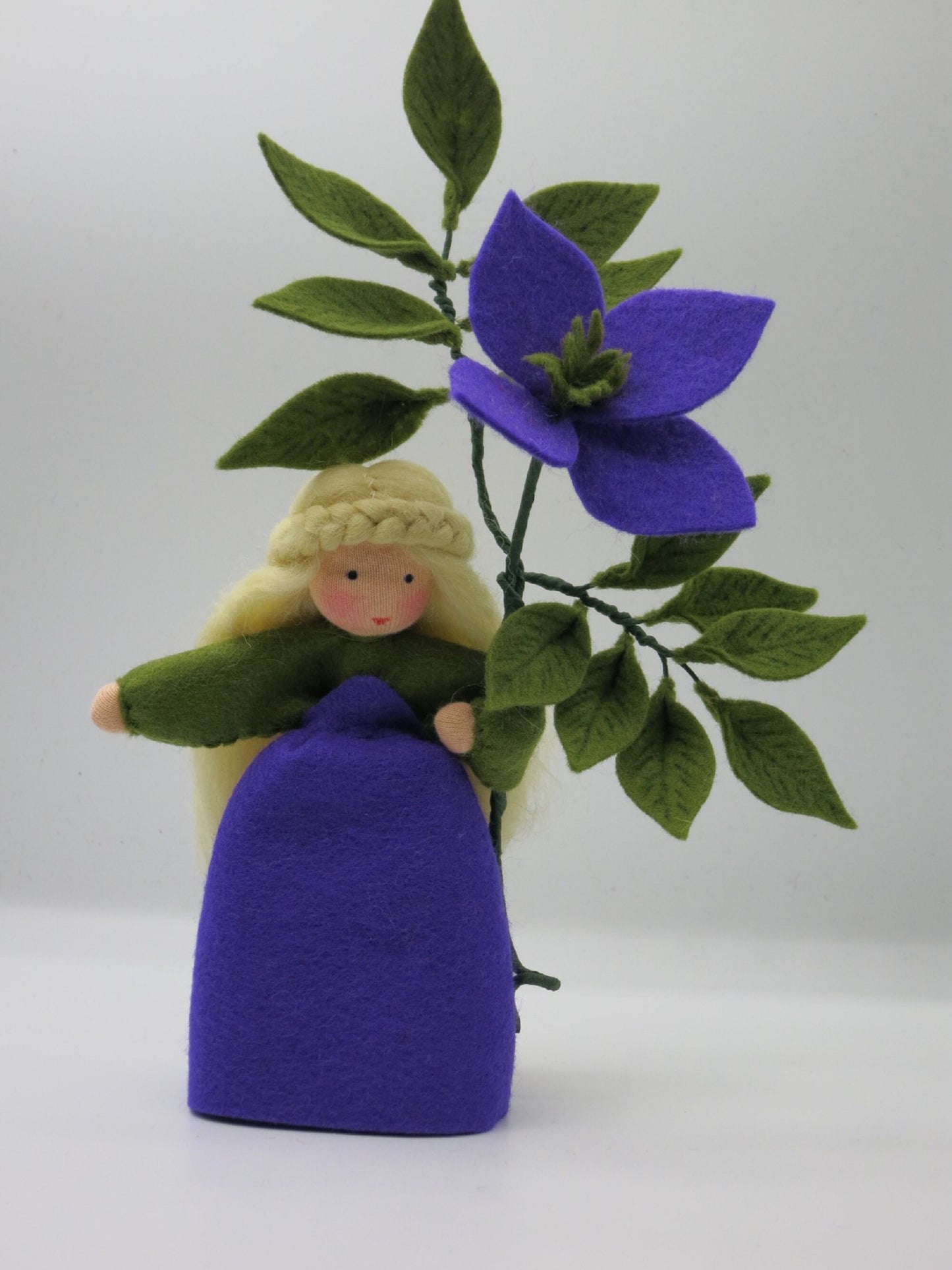 Handgefertigtes Clematis-Blumenkind mit violettem Filzkleid, großer Blüte und grünem Blätterzweig