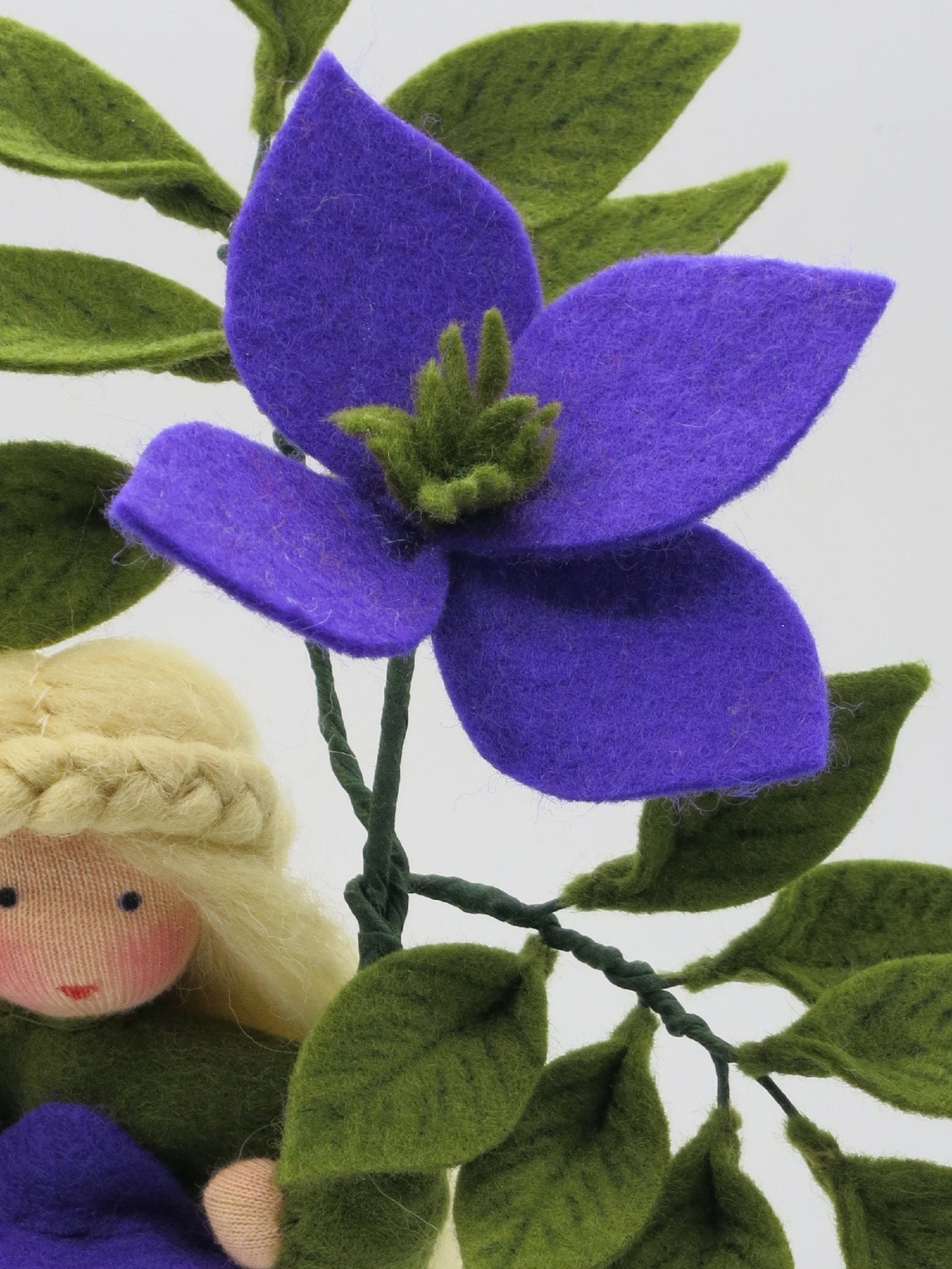 Detail der violetten Clematis-Blüte aus Filz mit grüner Mitte, Blättern und blondem Blumenkind