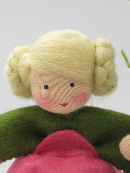 Porträt des Cosmea-Blumenkinds mit blonden geflochtenen Haarknoten, grünem Filzkragen und rosa Kleid