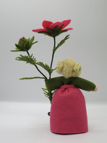 Rückansicht des Cosmea-Blumenkinds mit blonden Haarknoten, rosa Filzkleid und Schmuckkörbchen-Zweig