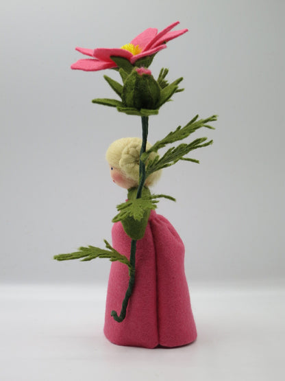 Seitliche Ansicht des Cosmea-Blumenkinds im rosa Filzkleid mit hoher Blüte, Knospe und feinem grünem Blattwerk