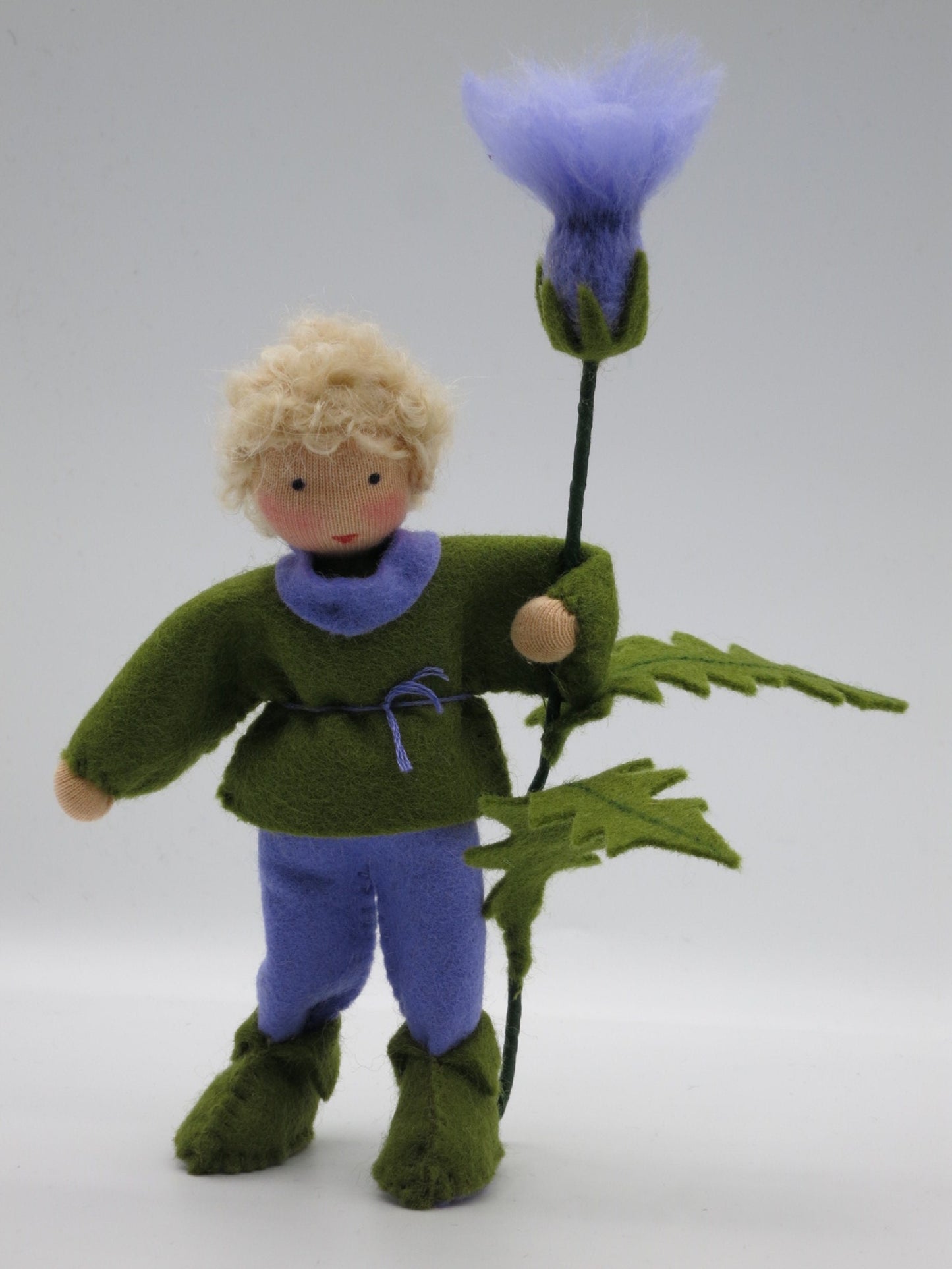 Distel-Junge frontal mit lilafarbener Hose, grünem Filzoberteil, gezackten Blättern und violetter Sommerblüte