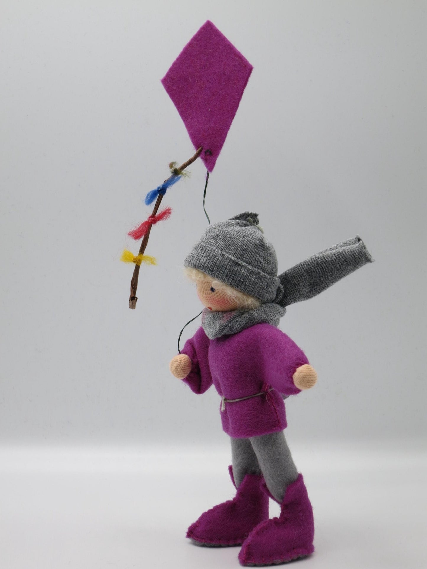 Seitliche Ansicht des Drachenkindes mit violettem Winddrachen, buntem Schweif und grau-lila Filzkleidung