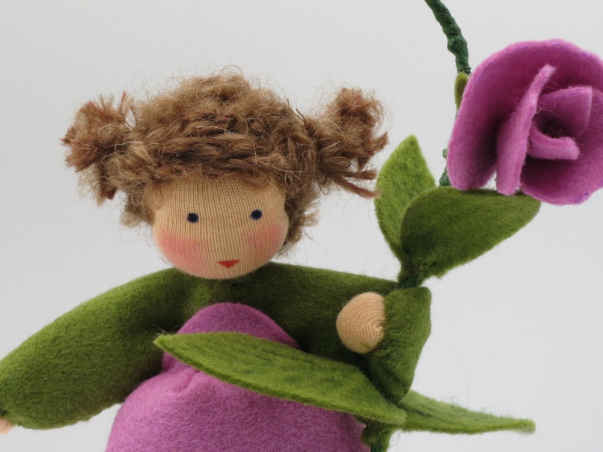 Porträt des handgefertigten Duftwicken-Blumenkindes mit braunen Locken, grünen Blättern und lila Filzblüte