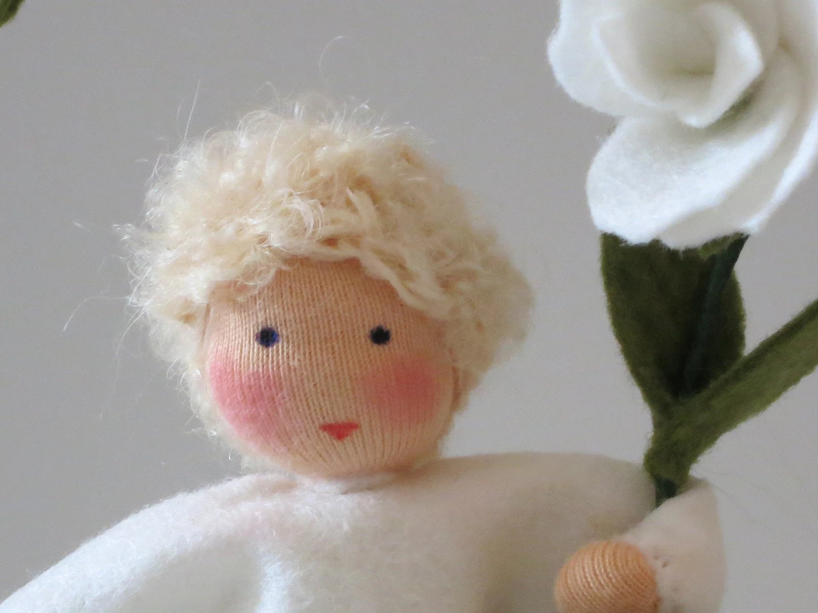 Detailaufnahme des Duftwicken-Jungen mit blondem Lockenhaar, handbemaltem Gesicht und weißer Filzblüte