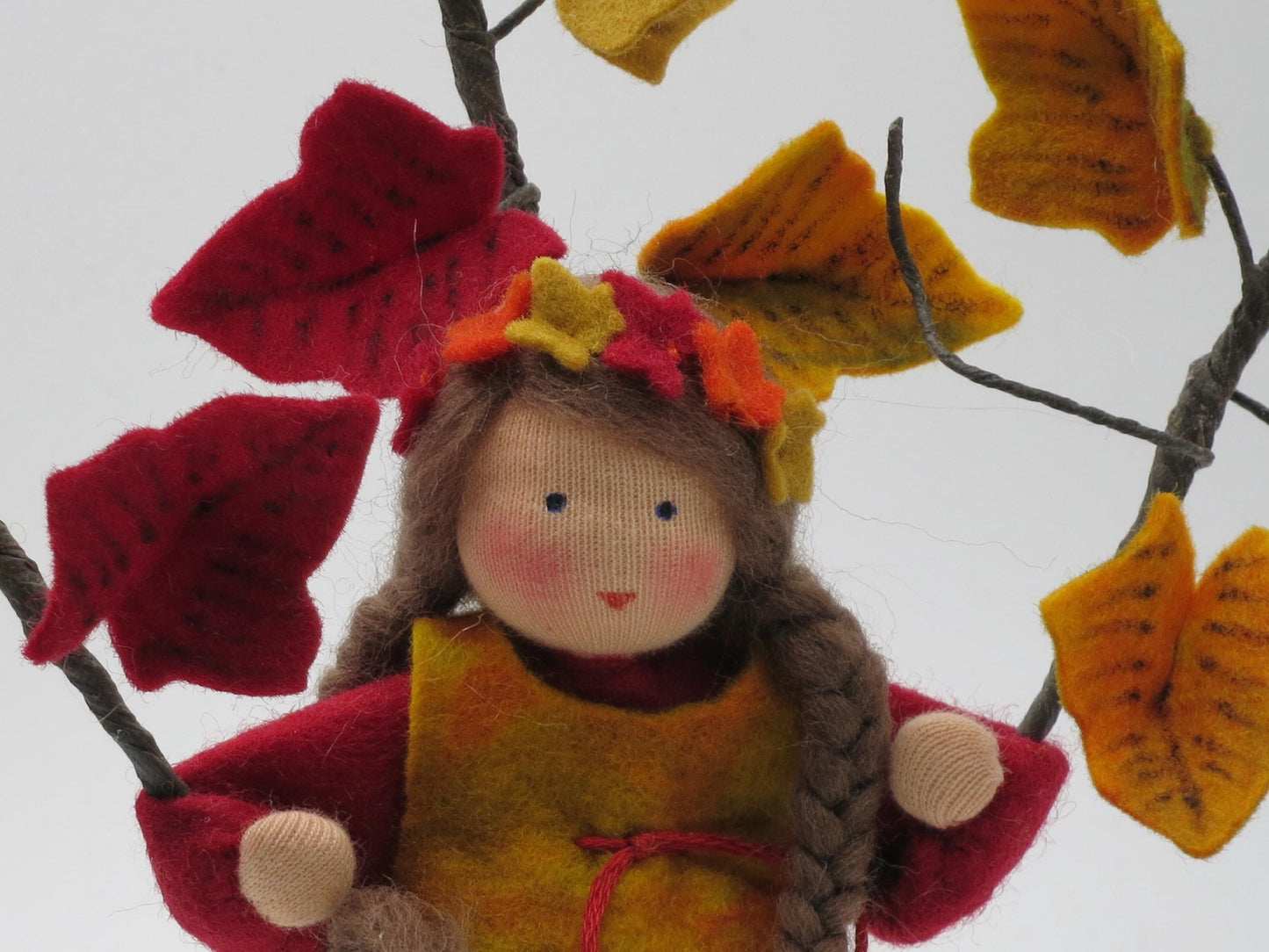 Herbstporträt des handgefertigten Efeu-Blumenkindes mit braunen Zöpfen und rot-gelbem Filzlaub am Jahreszeitentisch