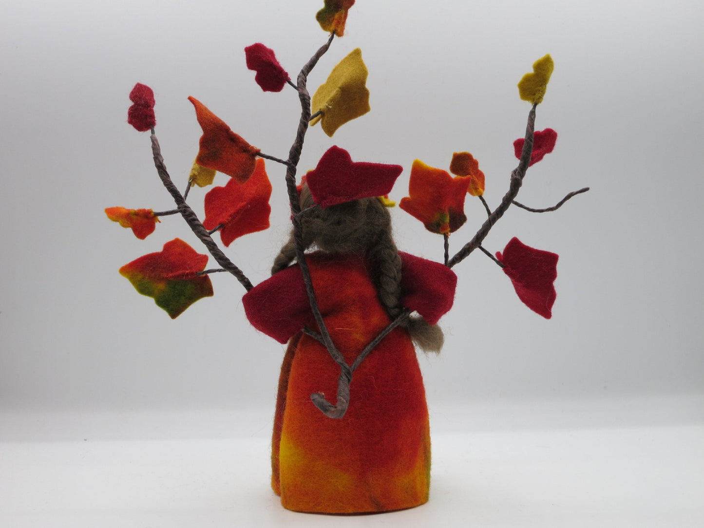 Rückansicht des handgefertigten Efeu-Blumenkindes mit braunem Haar, buntem Filzkleid und verzweigten Herbstblättern