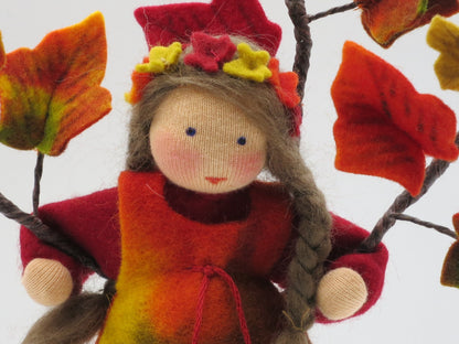 Porträt des handgefertigten Efeu-Blumenkindes mit langem braunem Zopf, Herbstlaub und rot-gelbem Filzkleid