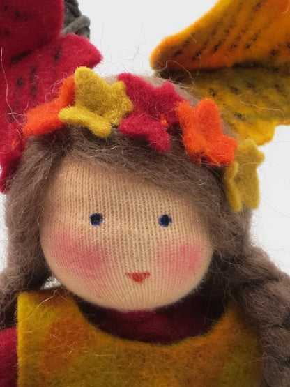 Detailaufnahme des Efeu-Blumenkindes mit braunem Haar, handbemaltem Gesicht und Kranz aus rotem und gelbem Filzlaub