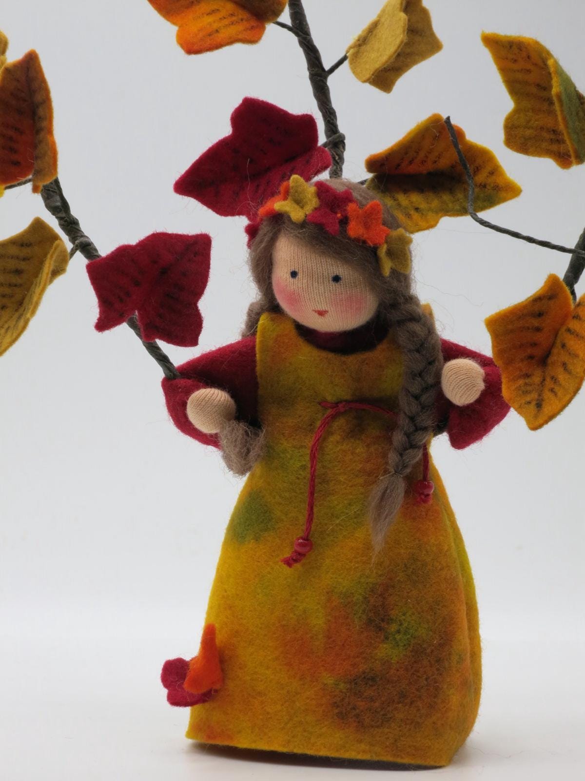 Frontalansicht des Efeu-Blumenkindes mit langen braunen Zöpfen, buntem Filzkleid und Herbstlaub für den Waldorf-Tisch