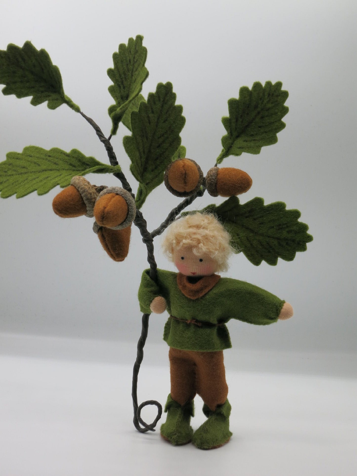 Eichel-Junge als handgefertigte Filzpuppe neben einem Eichenzweig mit Eicheln für den herbstlichen Jahreszeitentisch.