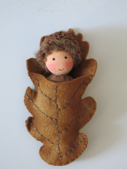 Braunhaariges Eichelbaby als handgefertigte Filzpuppe in einer Blätterhülle für den herbstlichen Jahreszeitentisch.