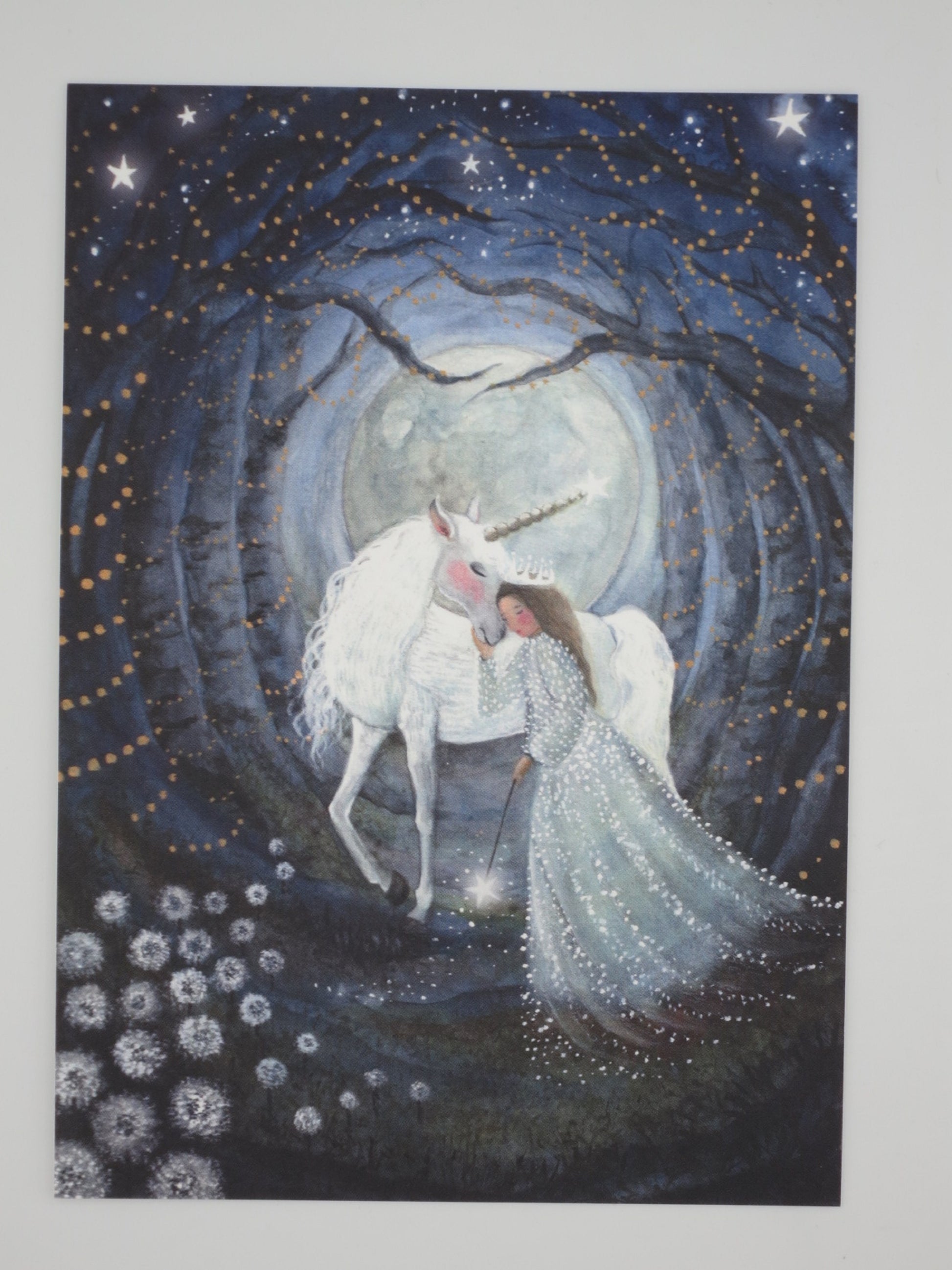 Einhorn-Postkarte für Kinder: Mädchen umarmt Einhorn mit Zauberstab vor Vollmond im Sternenwald