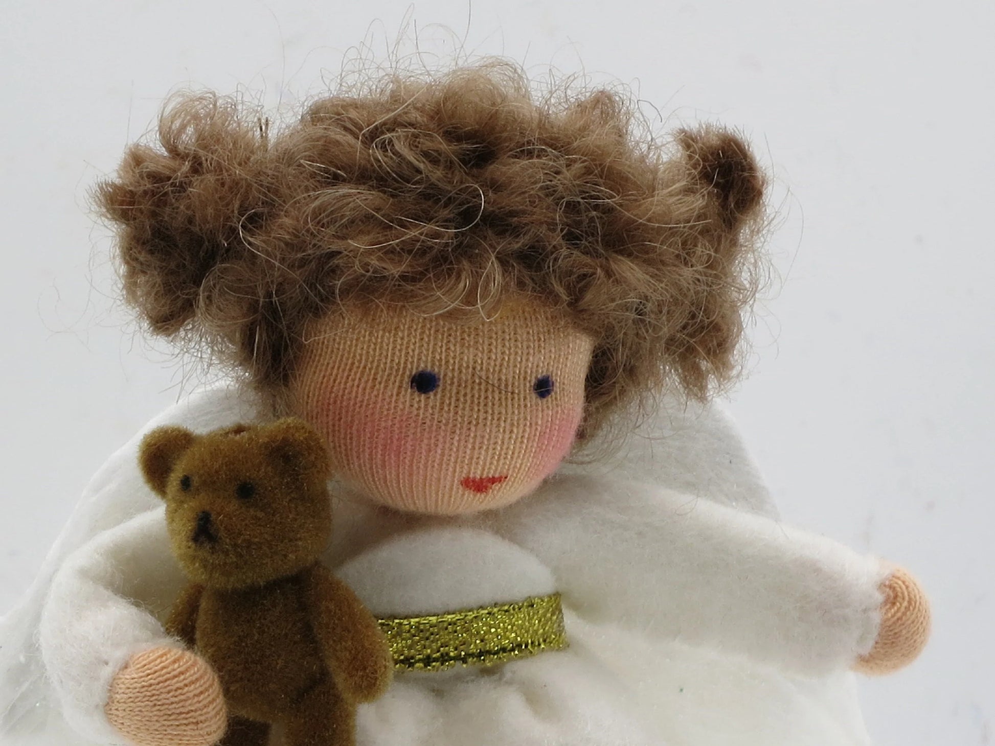 Detailansicht des handgefertigten Wollfilz-Engelchens mit braunem Lockenhaar, Teddy und weißen Flügeln.