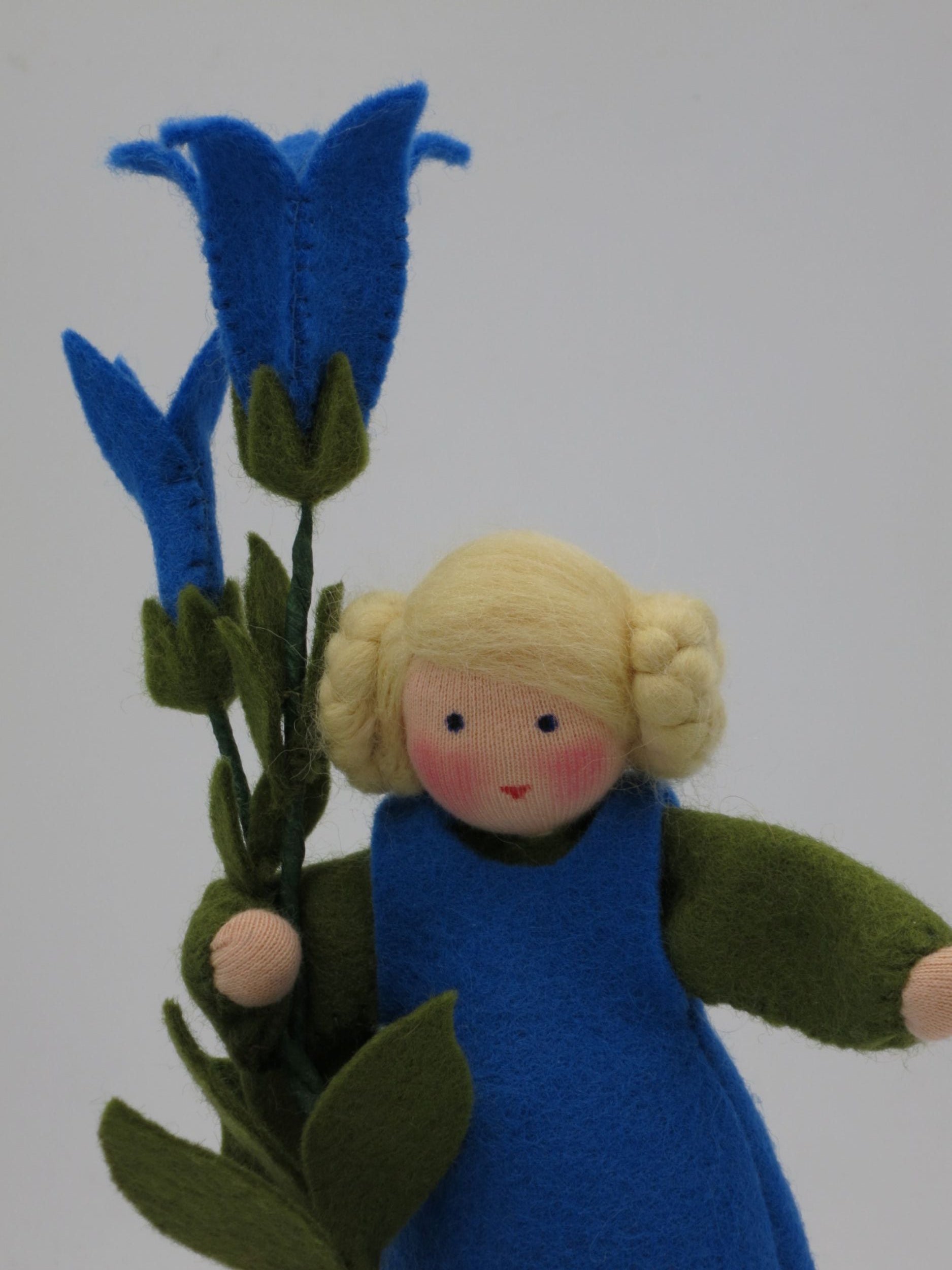 Porträt des handgefertigten Enzian-Blumenkinds mit blonden Zöpfen, blauem Wollfilzkleid und Enzianblüten.