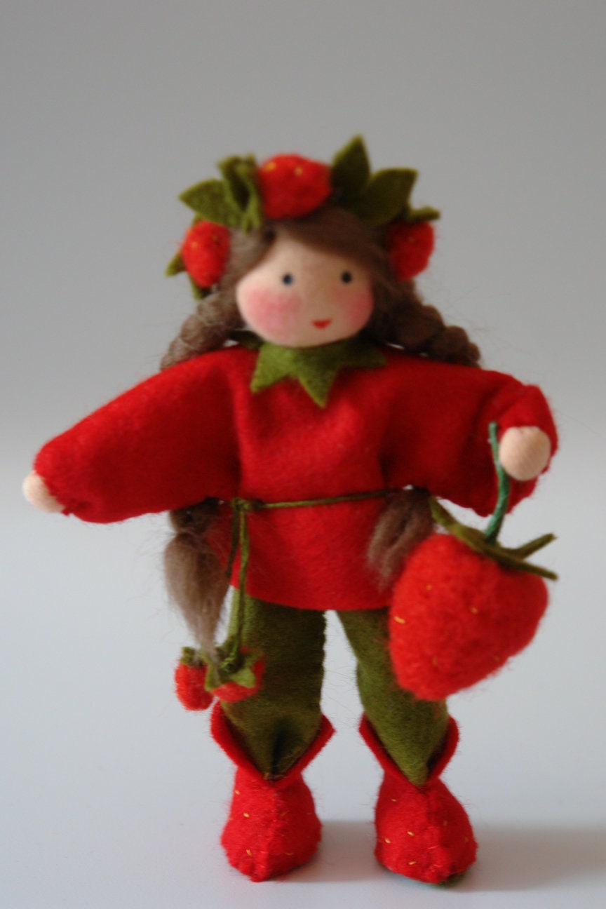 Frontalansicht des handgefertigten Erdbeer-Blumenkinds mit rotem Wollfilzkleid, Erdbeeren im Haar und großer Erdbeerfrucht.