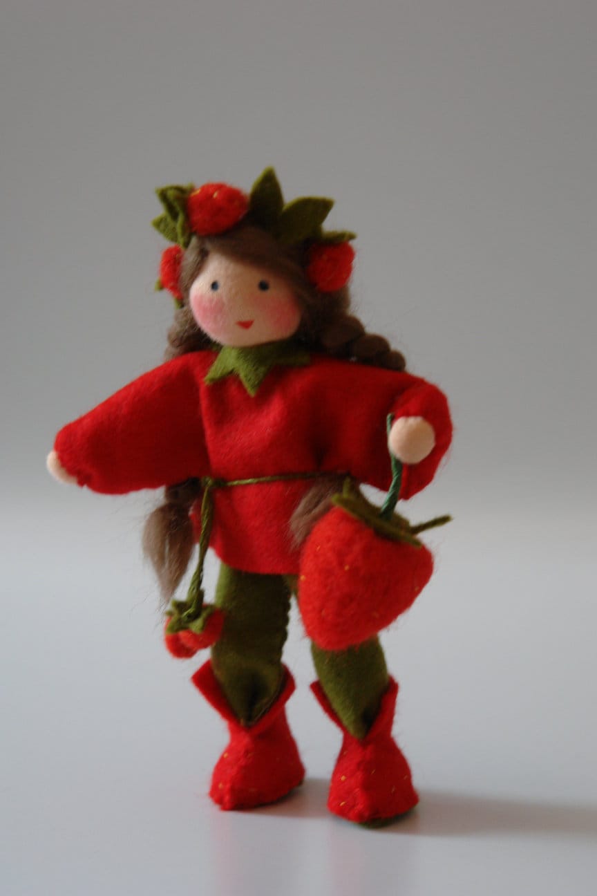 Erdbeer-Blumenkind aus Wollfilz mit roten Erdbeeren, rotem Kleid und großer Erdbeerfrucht als Sommerdekoration.