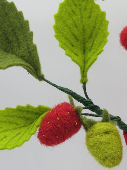 Detail des Erdbeerzweigs der Wollfilz-Erdbeerprinzessin mit roten und grünen Erdbeeren sowie Blättern.