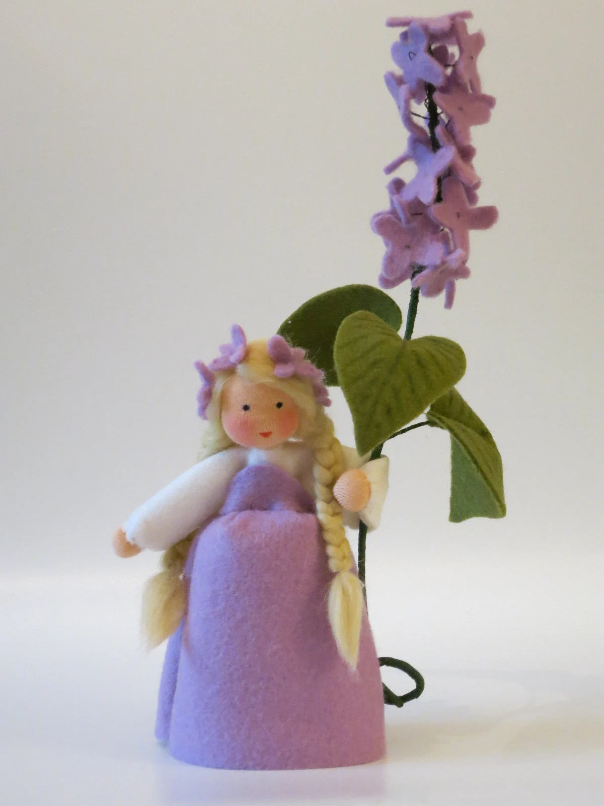 Handgefertigtes Flieder-Blumenkind aus Wollfilz mit lila Kleid, blondem Haar und Fliederzweig als Frühlingsdekoration.