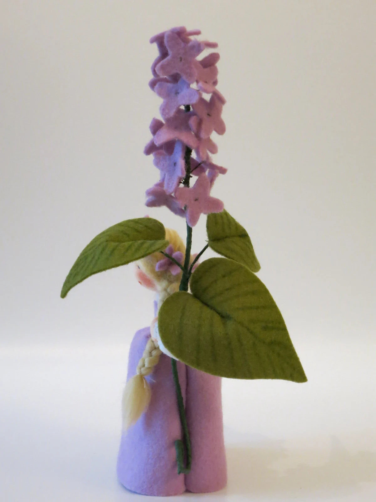 Seitenansicht des Flieder-Blumenkinds aus Wollfilz mit lila Kleid, Blätterzweig und zarten Fliederblüten.