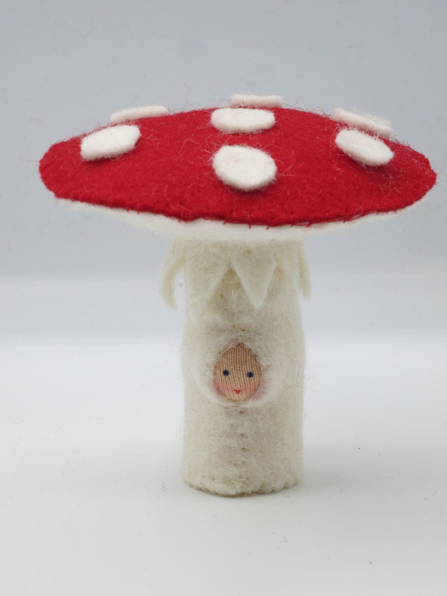 Handgefertigte Fliegenpilz-Pilzfigur aus Wollfilz mit rotem Hut, weißen Punkten und kleinem Gesicht im weißen Stiel.