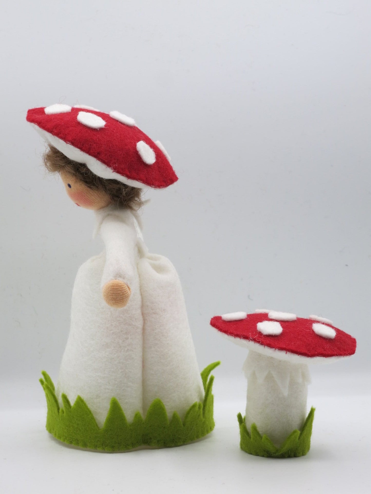 Seitenansicht des Fliegenpilz-Blumenkinds aus Wollfilz mit weißem Kleid, rotem Pilzhut und separatem Fliegenpilz.