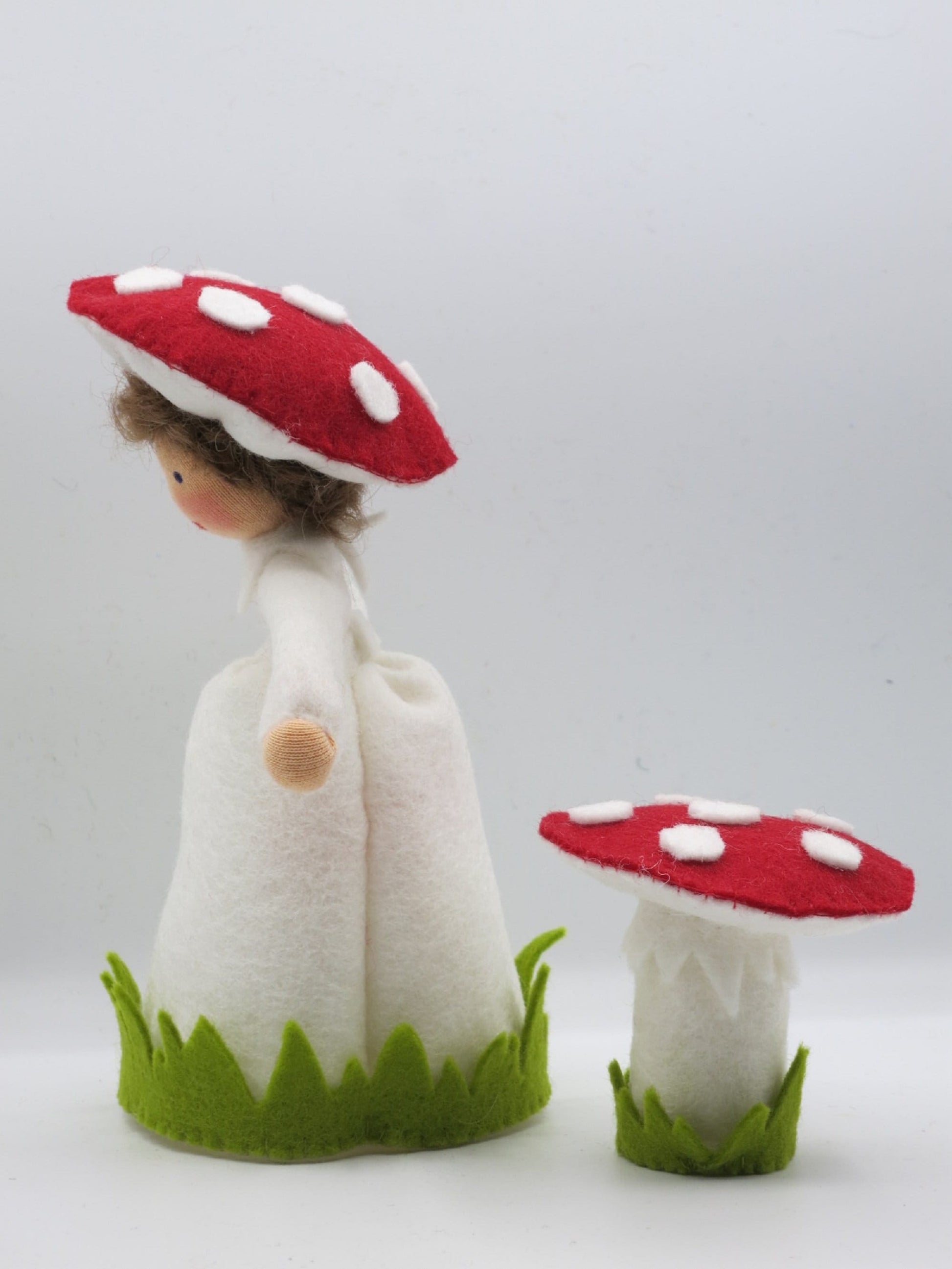 Seitenansicht des Fliegenpilz-Blumenkinds aus Wollfilz mit weißem Kleid, rotem Pilzhut und separatem Fliegenpilz.