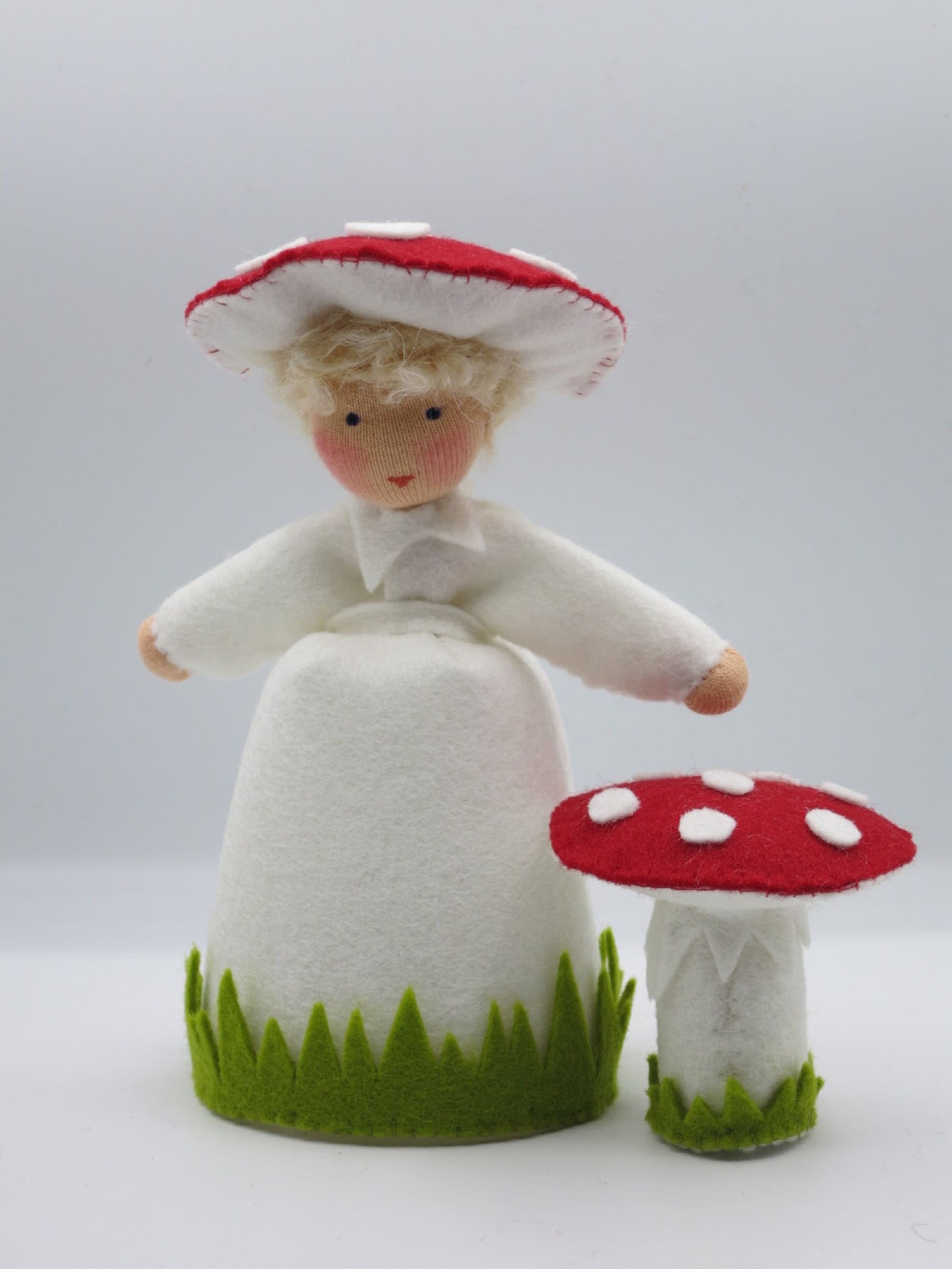 Frontalansicht des Fliegenpilz-Blumenkinds aus Wollfilz mit weißem Gewand, rot-weißem Pilzhut und kleinem Fliegenpilz.