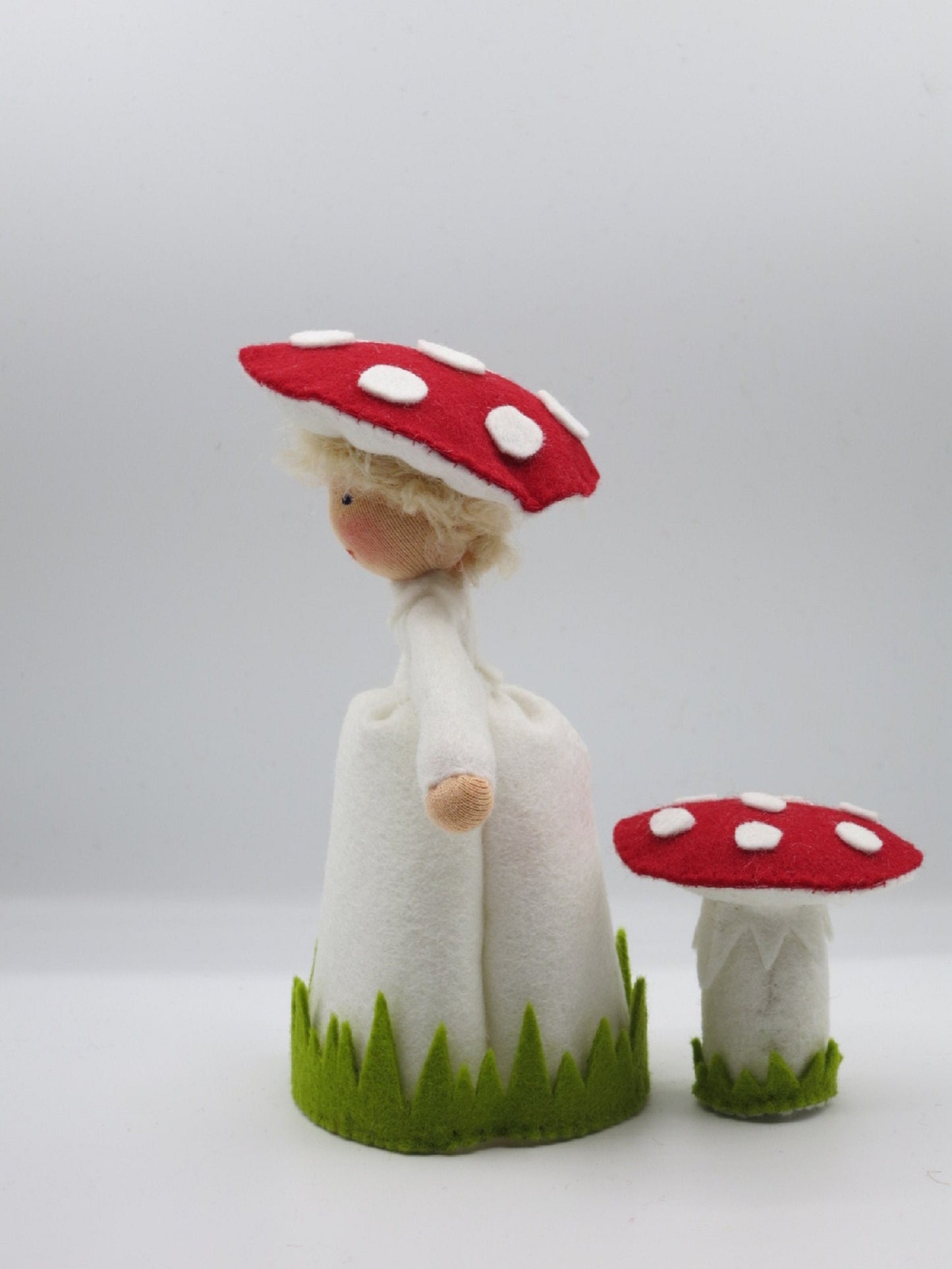 Seitenansicht des handgefertigten Fliegenpilz-Blumenkinds aus Wollfilz mit Pilzhut und kleinem rot-weißen Fliegenpilz.