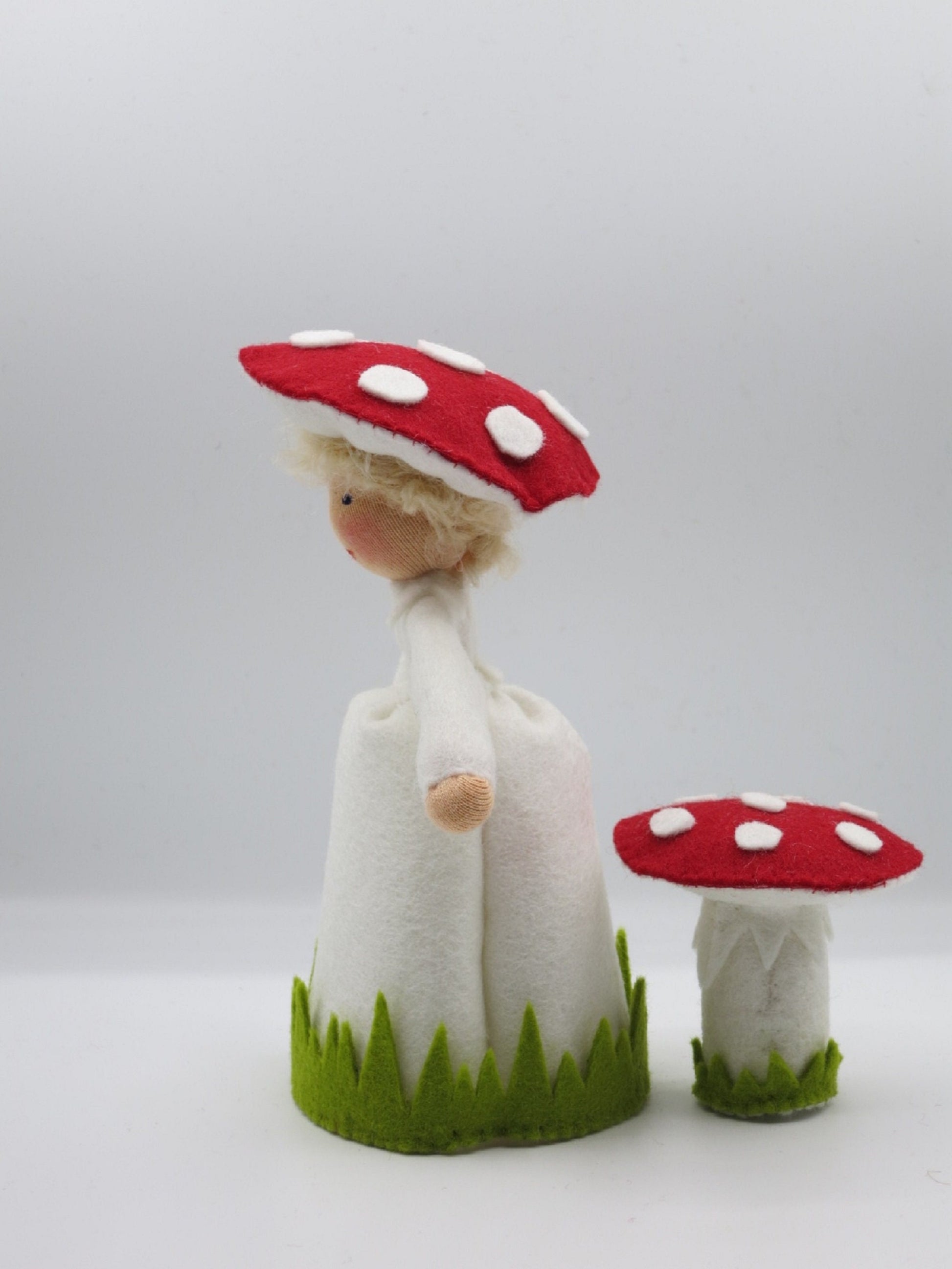 Seitenansicht des handgefertigten Fliegenpilz-Blumenkinds aus Wollfilz mit Pilzhut und kleinem rot-weißen Fliegenpilz.