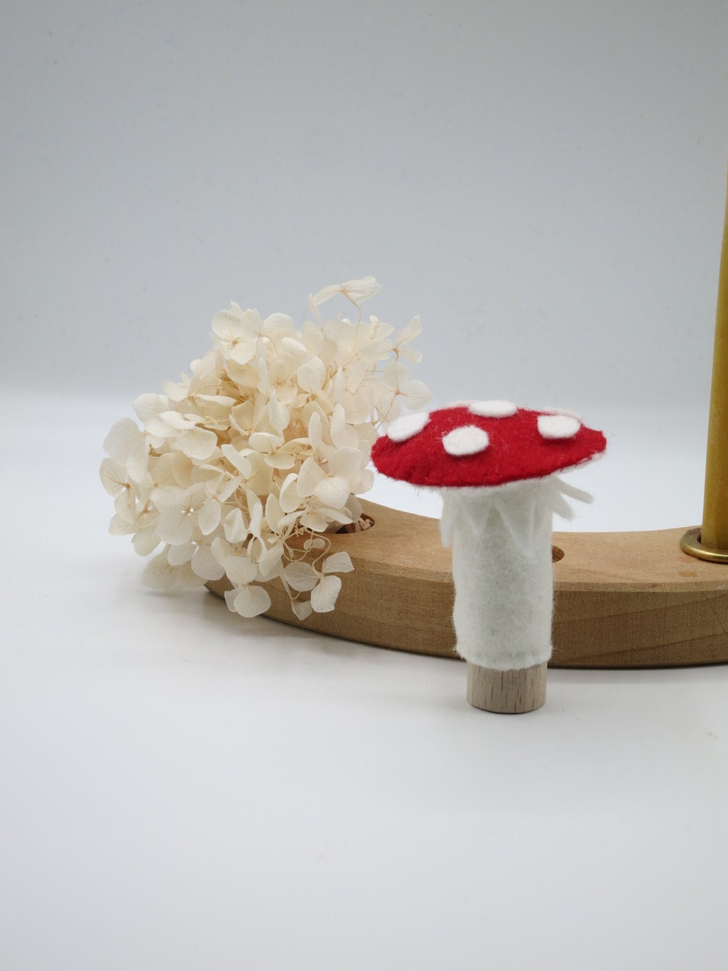 Fliegenpilz-Stecker aus Wollfilz vor einem Holz-Geburtstagsring mit Trockenblumen und Kerzenhalter als Tischdekoration.