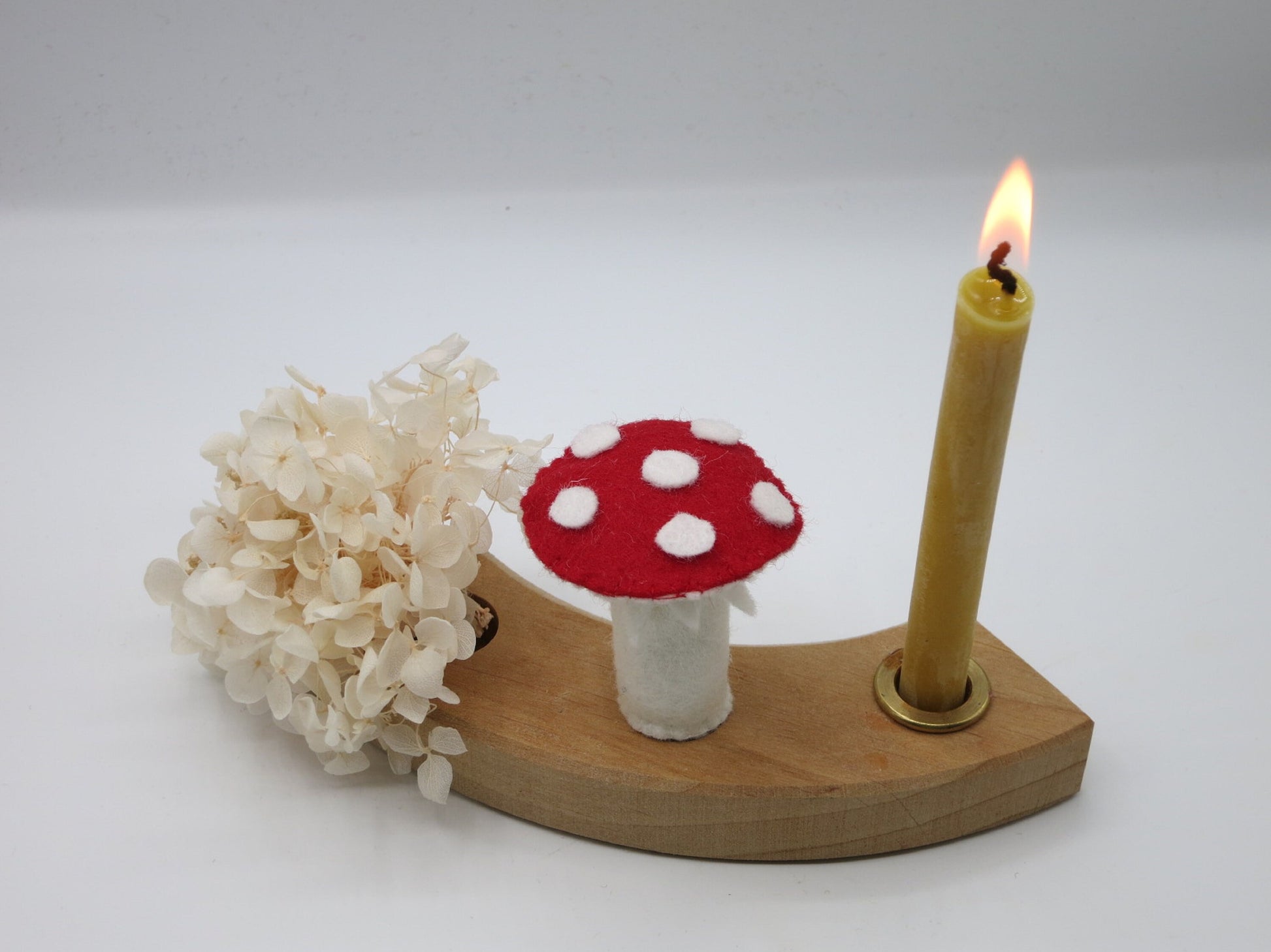 Fliegenpilz-Stecker aus Wollfilz im Holz-Geburtstagsring mit brennender Kerze und weißen Trockenblumen.