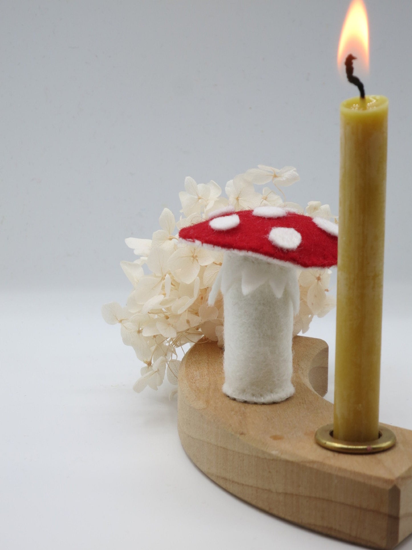 Handgefertigter Fliegenpilz-Stecker aus Wollfilz im Holz-Kerzenring mit Kerze und weißen Trockenblumen als Herbstdekoration.