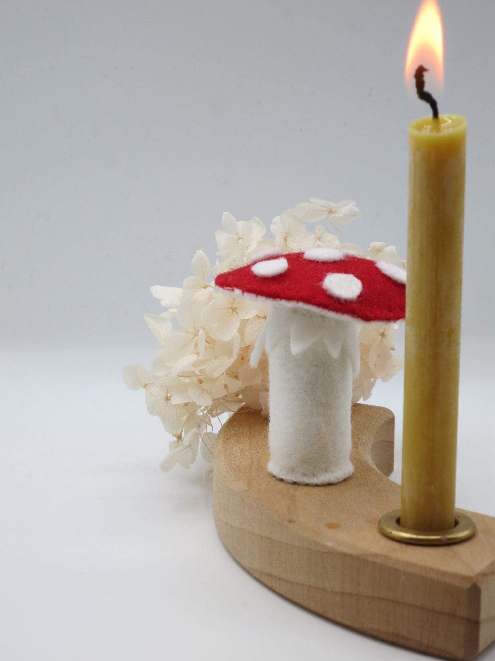 Handgefertigter Fliegenpilz-Stecker aus Wollfilz im Holz-Kerzenring mit Kerze und weißen Trockenblumen als Herbstdekoration.