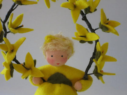 Detailansicht des Forsythien-Blumenkinds aus Wollfilz mit blondem Haar und Kranz aus gelben Forsythienblüten.