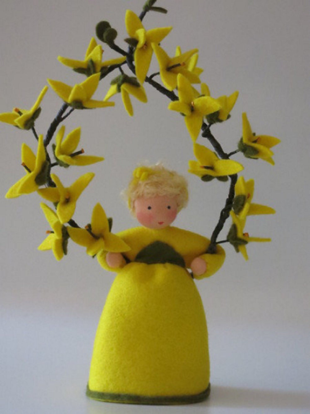 Handgefertigtes Forsythien-Blumenkind aus Wollfilz im Kranz aus gelben Forsythienblüten als Frühlingsdekoration.