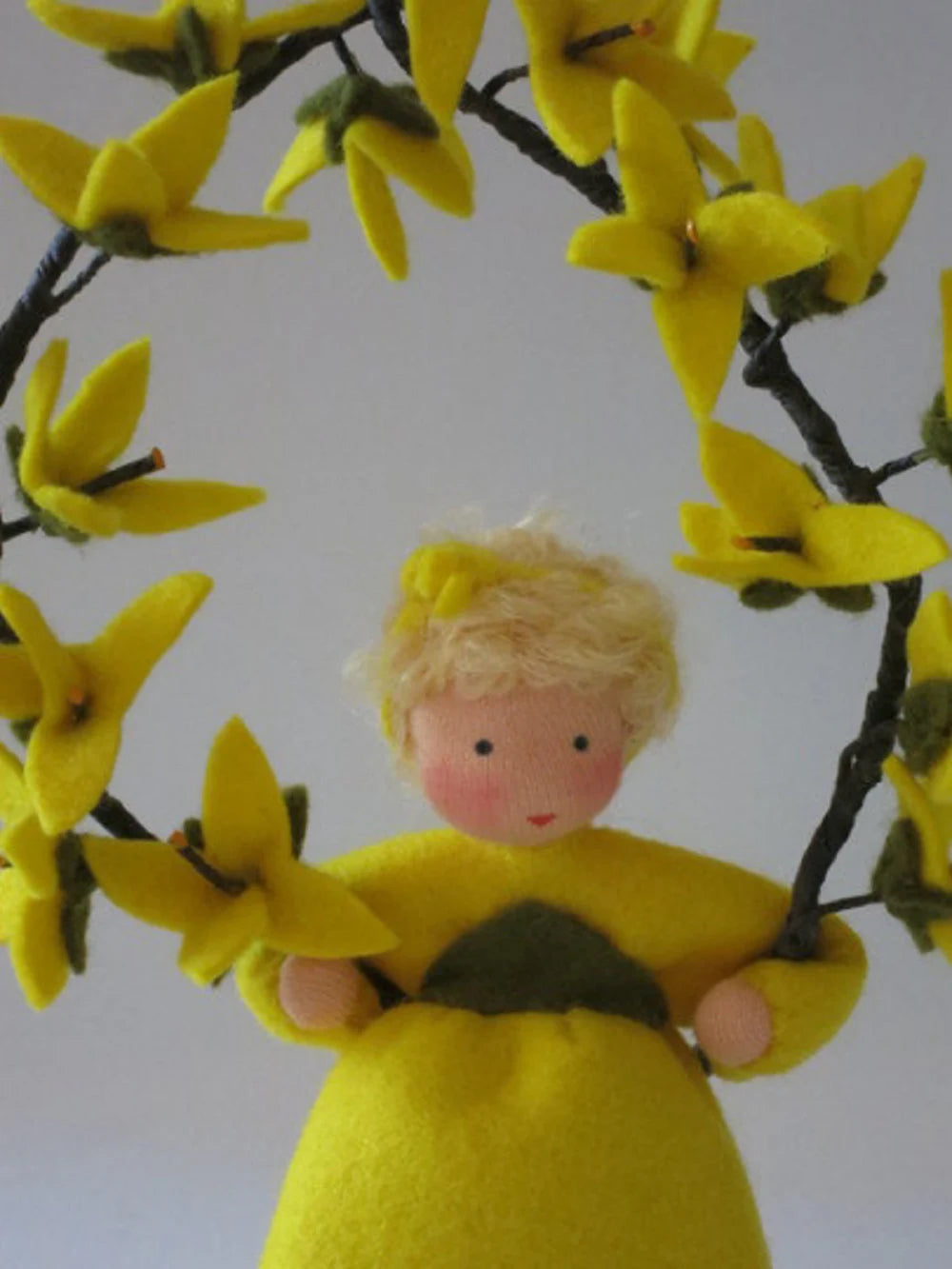 Porträt des handgefertigten Forsythien-Blumenkinds aus Wollfilz im Rahmen gelber Zweigblüten.