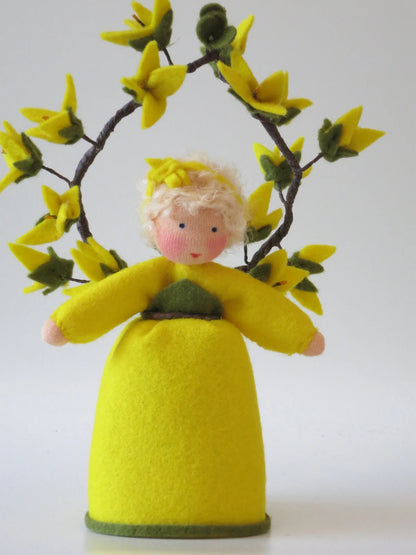 Frontalansicht des Forsythien-Blumenkinds aus Wollfilz mit gelbem Kleid, grüner Blätterapplikation und gelben Zweigblüten.