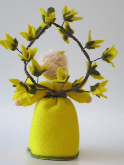 Rückansicht des Forsythien-Blumenkinds aus Wollfilz mit gelbem Kleid und Kranz aus Forsythienzweigen.