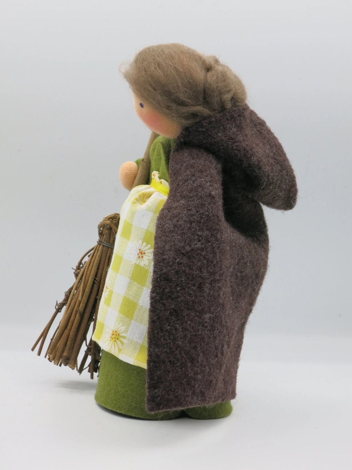 Seitenansicht von Fräulein Tau aus Wollfilz mit braunem Umhang, Besen, grünem Kleid und gelb-weißem Schürzchen.